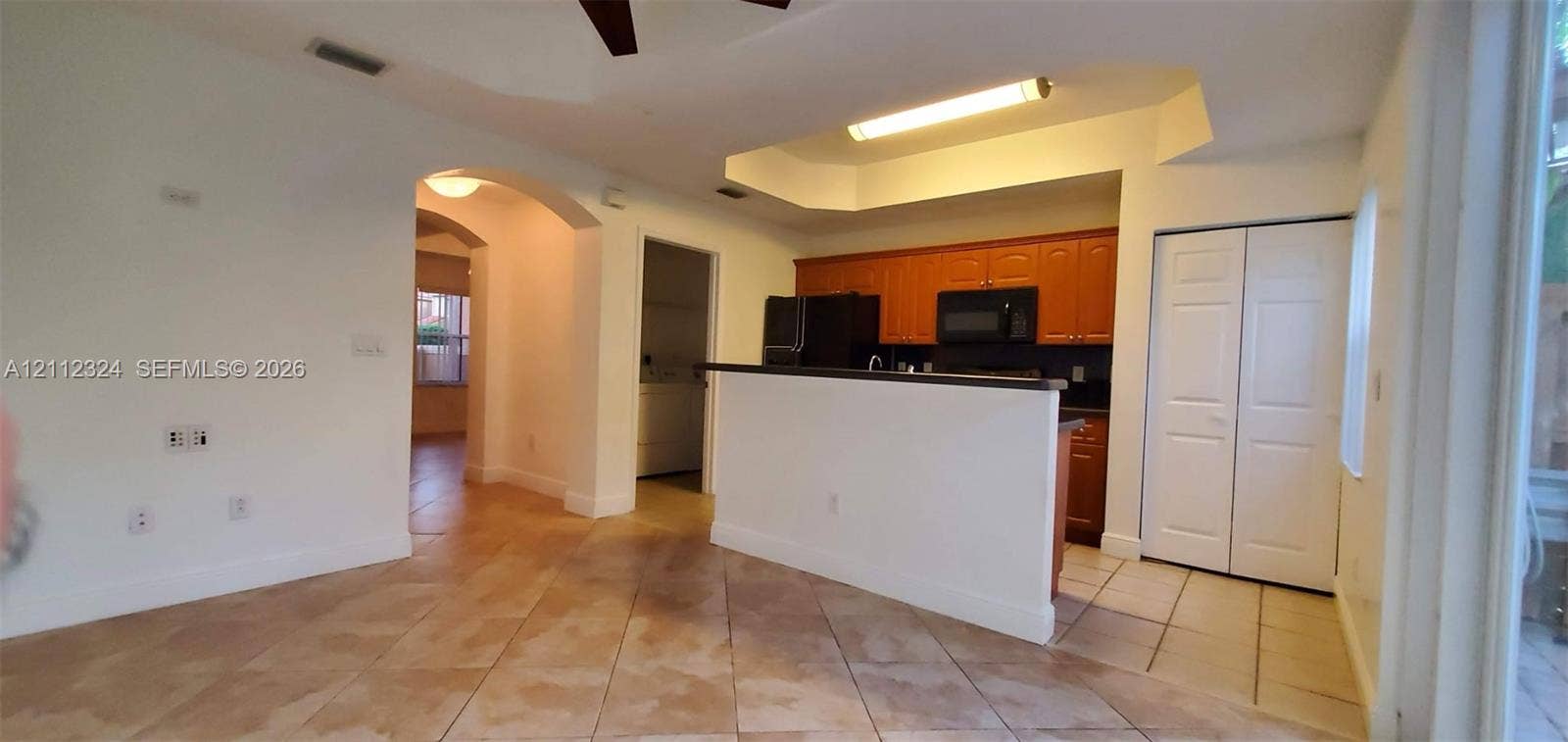 Kitchen featuring a peninsula counter, wood-finish cabinetry, built-in microwave, tiled flooring, and a tray ceiling with recessed lighting
