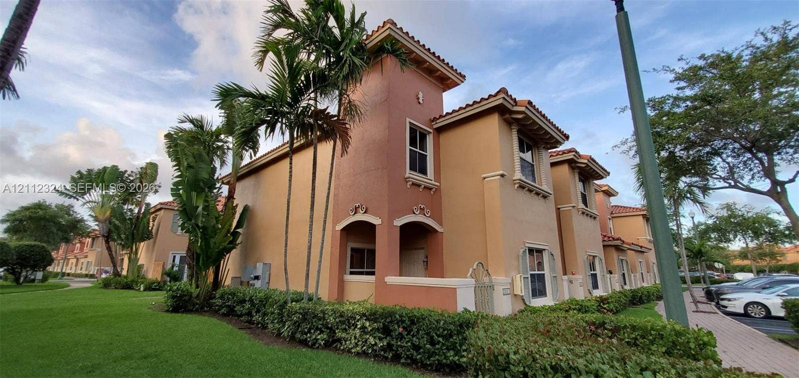 Multi-story exterior featuring a stucco facade, tiled roof, decorative archways, and manicured tropical landscaping