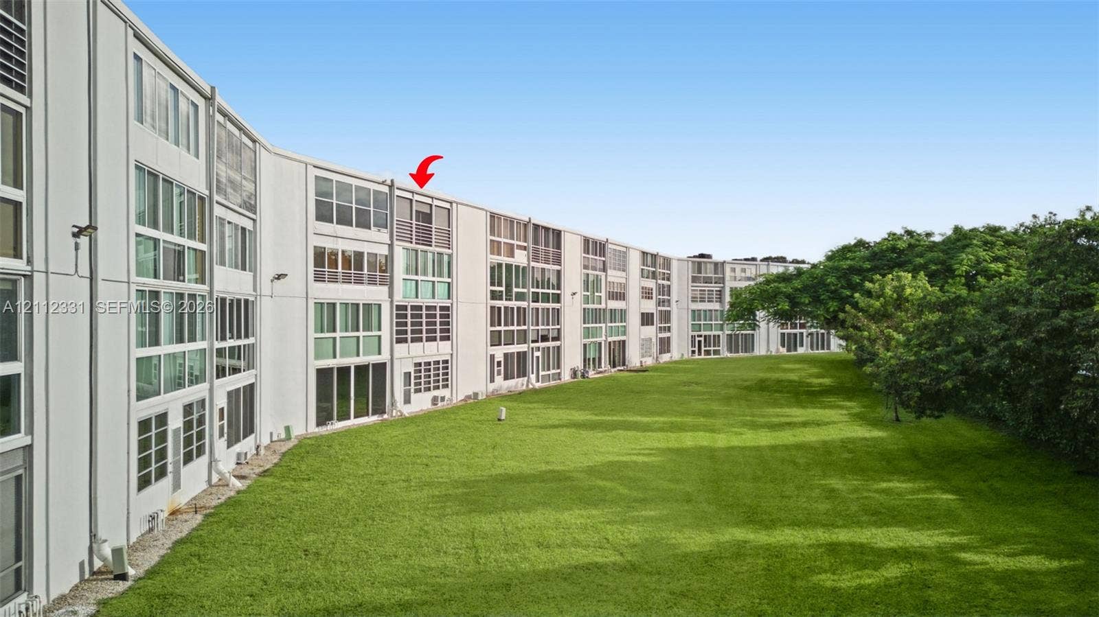 4025 Upminster K, #4025, Deerfield Beach, FL 33442 Multi-story exterior featuring a grid-pattern facade, extensive floor-to-ceiling glass windows, integrated privacy screens, and an expansive lawn bordered by mature trees