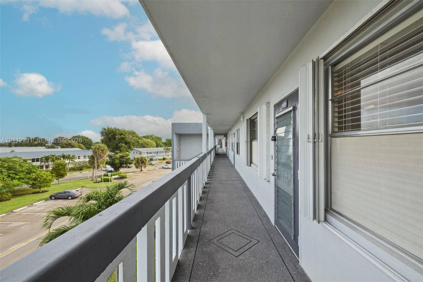 4025 Upminster K, #4025, Deerfield Beach, FL 33442 Covered exterior walkway featuring a textured concrete floor, metal railings, and integrated security door screening