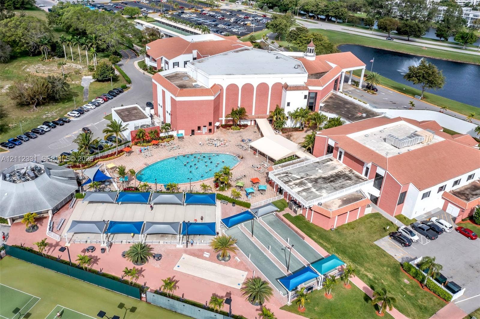 4025 Upminster K, #4025, Deerfield Beach, FL 33442 Aerial perspective of the property featuring a swimming pool, multiple tennis courts, shaded patio structures, and dedicated shuffleboard areas
