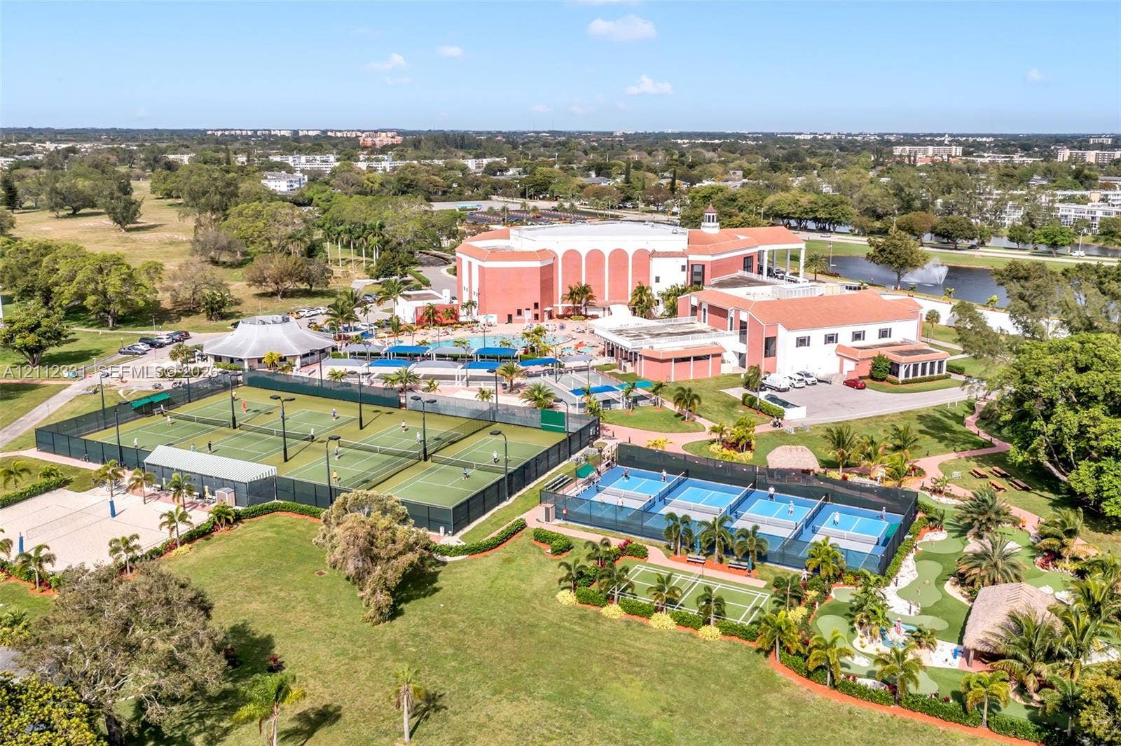 4025 Upminster K, #4025, Deerfield Beach, FL 33442 Aerial perspective of a multi-facility recreational complex featuring multiple tennis courts, pickleball courts, a miniature golf course, and a swimming pool