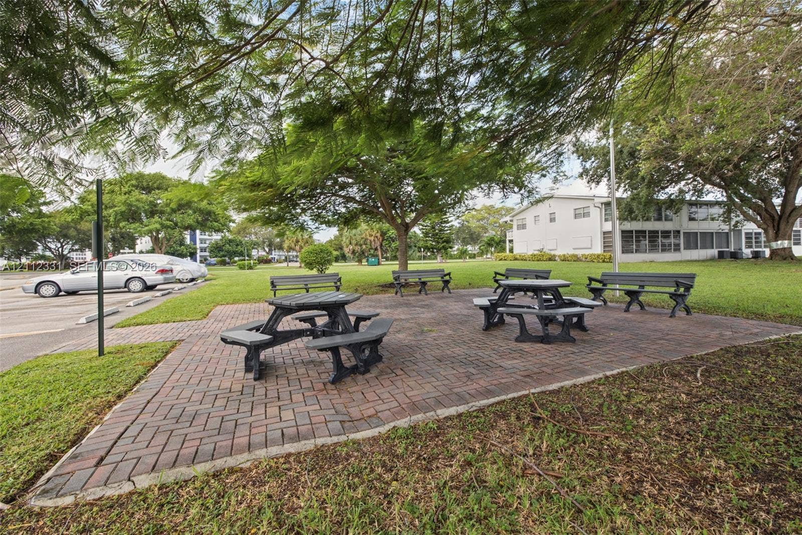 4025 Upminster K, #4025, Deerfield Beach, FL 33442 Outdoor common area featuring a brick-paver patio, permanent benches, and mature shade trees