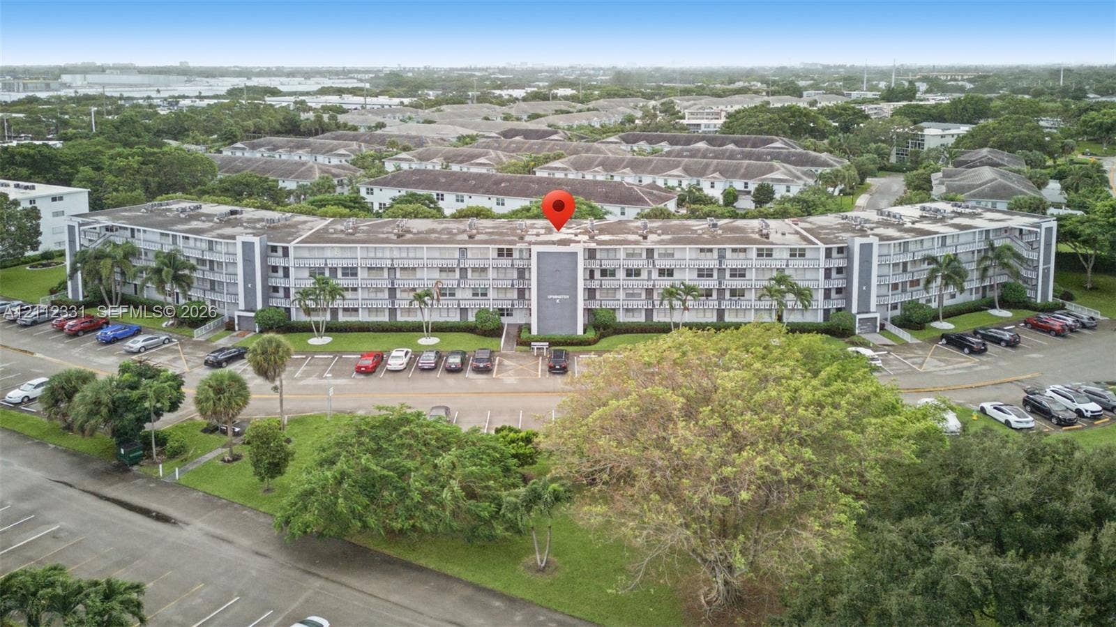 4025 Upminster K, #4025, Deerfield Beach, FL 33442 Multi-story residential building featuring a concrete facade, balcony rows, dedicated surface parking, and mature palm trees
