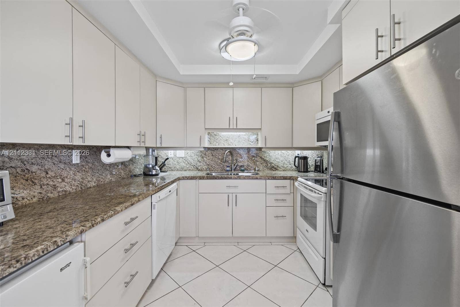 4025 Upminster K, #4025, Deerfield Beach, FL 33442 Kitchen featuring light-toned cabinetry with brushed metal pulls, stone-composite countertops, stainless steel refrigerator, white appliances, and diagonal-set tile flooring