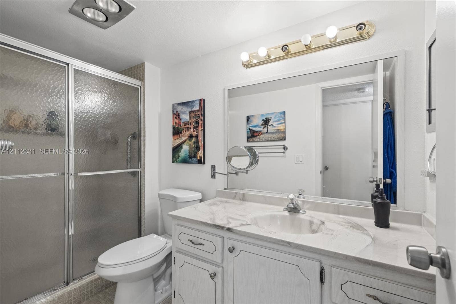4025 Upminster K, #4025, Deerfield Beach, FL 33442 Bathroom featuring a vanity with a stone-top surface and integrated basin, a large wall-mounted mirror, a multi-bulb vanity light fixture, and a glass-enclosed shower with metal frame