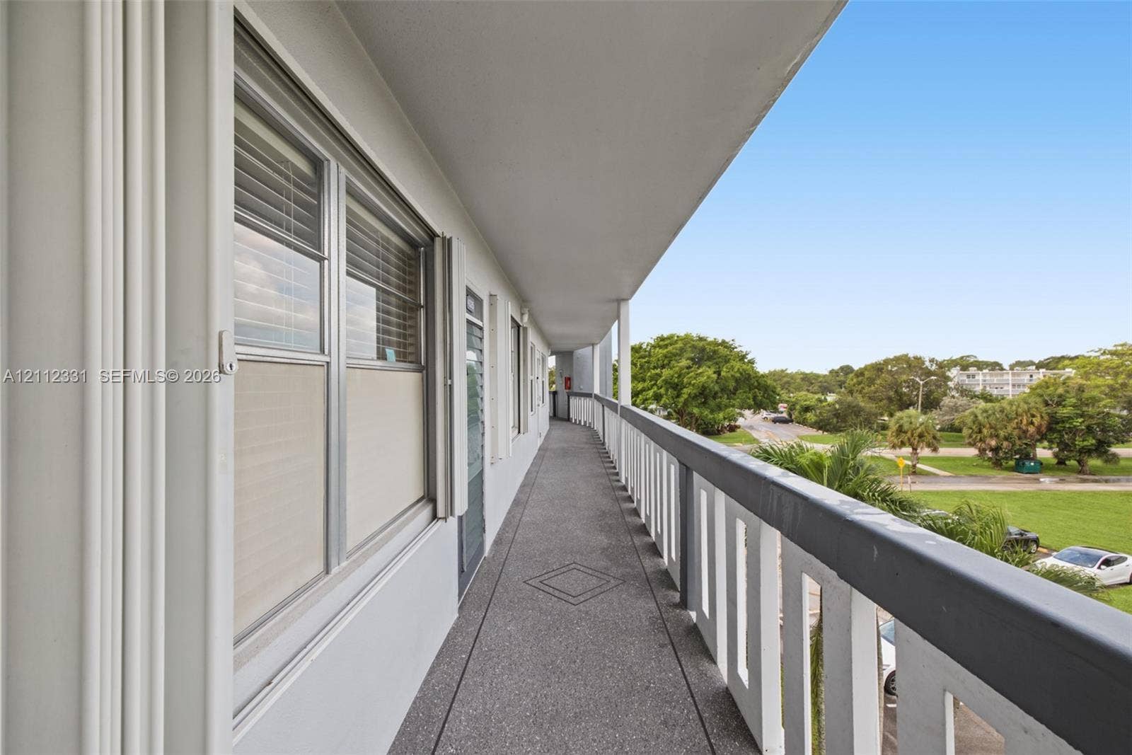 4025 Upminster K, #4025, Deerfield Beach, FL 33442 Covered exterior walkway featuring a textured concrete surface, metal railing, and recessed wall-mounted lighting