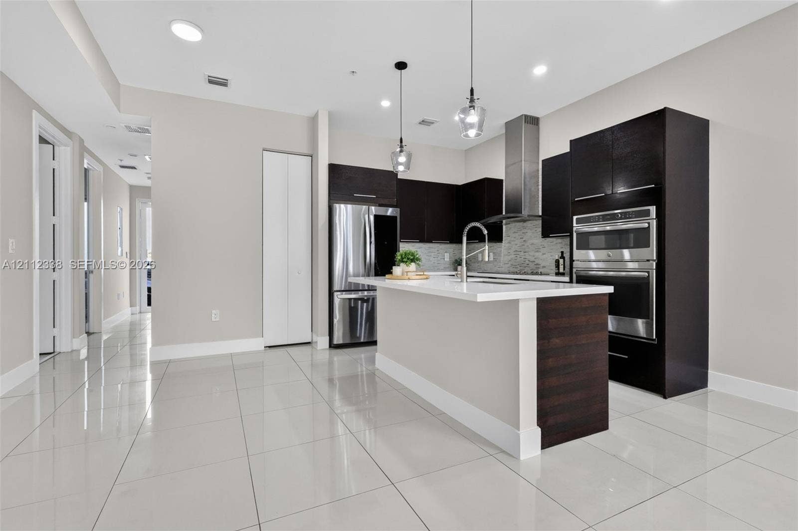 10305 NW 63rd Terrace, #102, Doral, FL 33178 Kitchen featuring dark wood-finish cabinetry, a central island with white countertop, stainless steel double wall ovens, a stainless steel range hood, and tile flooring