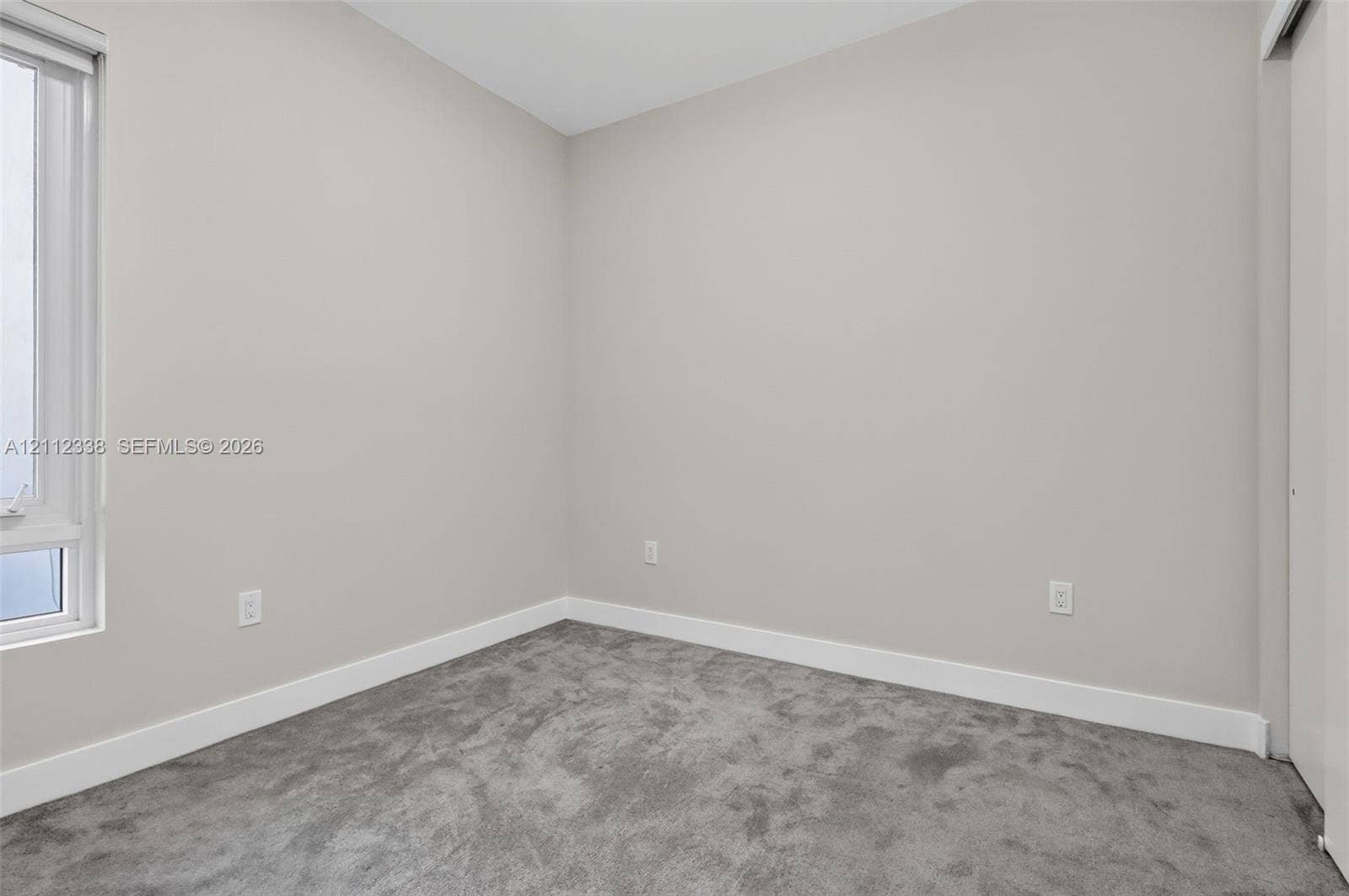 10305 NW 63rd Terrace, #102, Doral, FL 33178 Neutral-toned interior space featuring plush carpeting, soft gray wall paint, and a single-pane vertical window with integrated blinds
