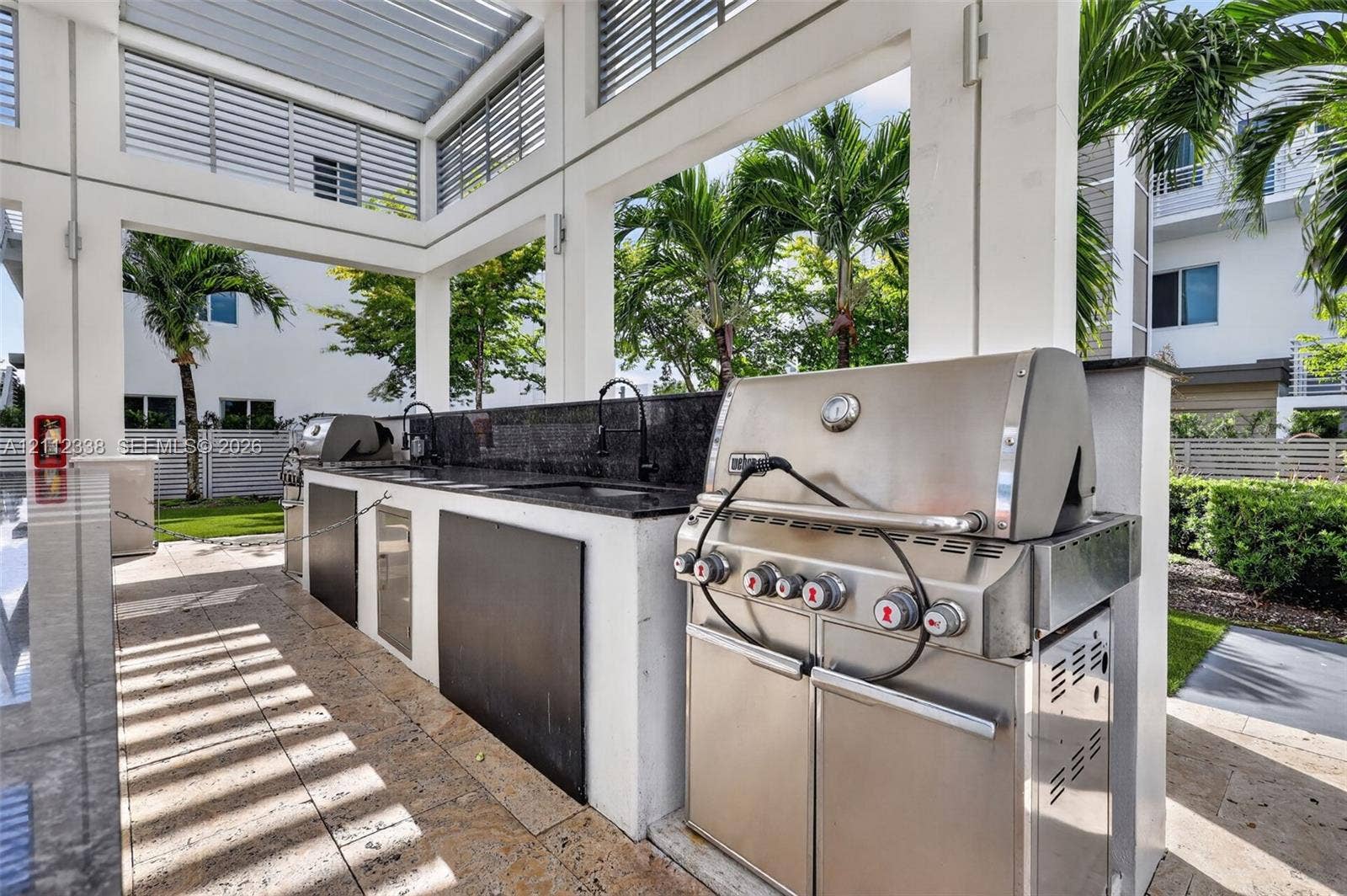 10305 NW 63rd Terrace, #102, Doral, FL 33178 Covered outdoor kitchen featuring a stainless steel grill, stone countertop, built-in sink, and stone-tile flooring