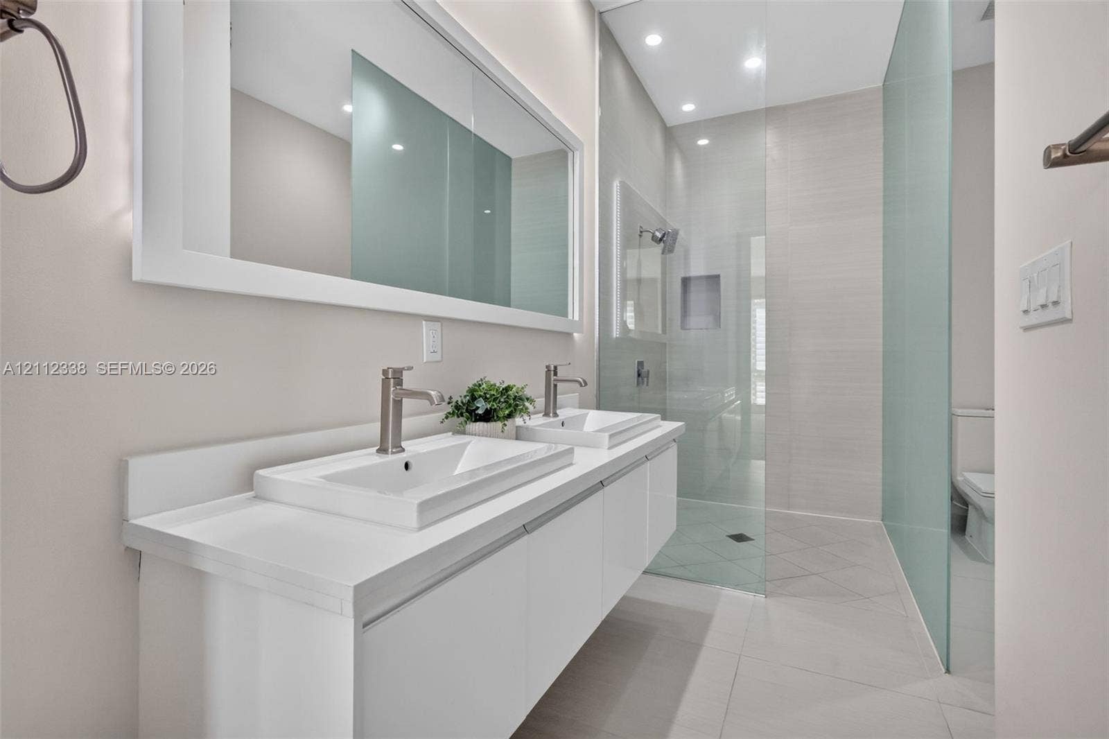 10305 NW 63rd Terrace, #102, Doral, FL 33178 Double floating vanity with rectangular sinks, integrated mirror, glass-enclosed shower featuring a recessed niche, and stone-finish floor tiling
