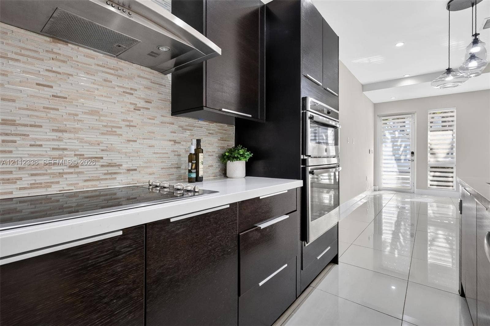 10305 NW 63rd Terrace, #102, Doral, FL 33178 Kitchen featuring dark-finish flat-panel cabinetry, light-toned stone countertops, a linear mosaic tile backsplash, stainless steel built-in double ovens, and large-format porcelain tile flooring