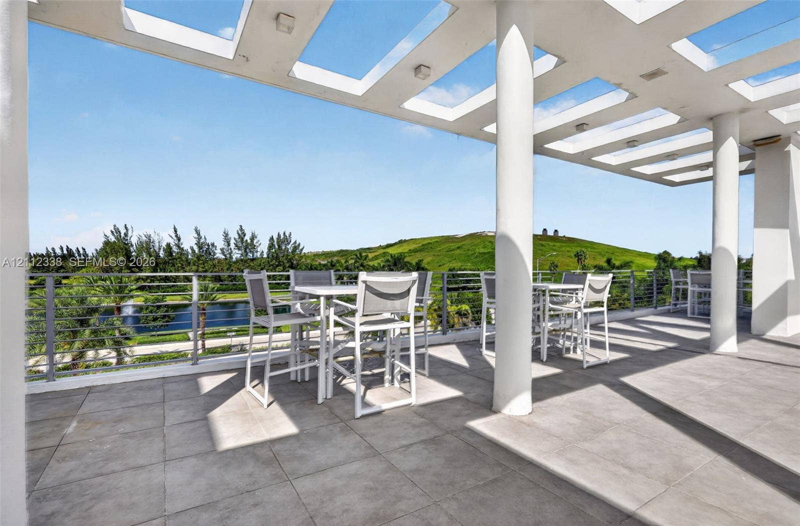 10305 NW 63rd Terrace, #102, Doral, FL 33178 Covered terrace featuring a pergola-style ceiling, structural support columns, oversized tile flooring, and a metal cable railing system overlooking a landscape backdrop