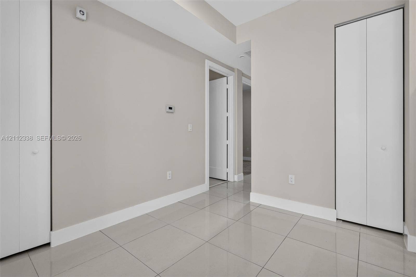 10305 NW 63rd Terrace, #102, Doral, FL 33178 Interior space featuring large-format neutral tile flooring, two sets of white bi-fold closet doors, and smooth wall finishes