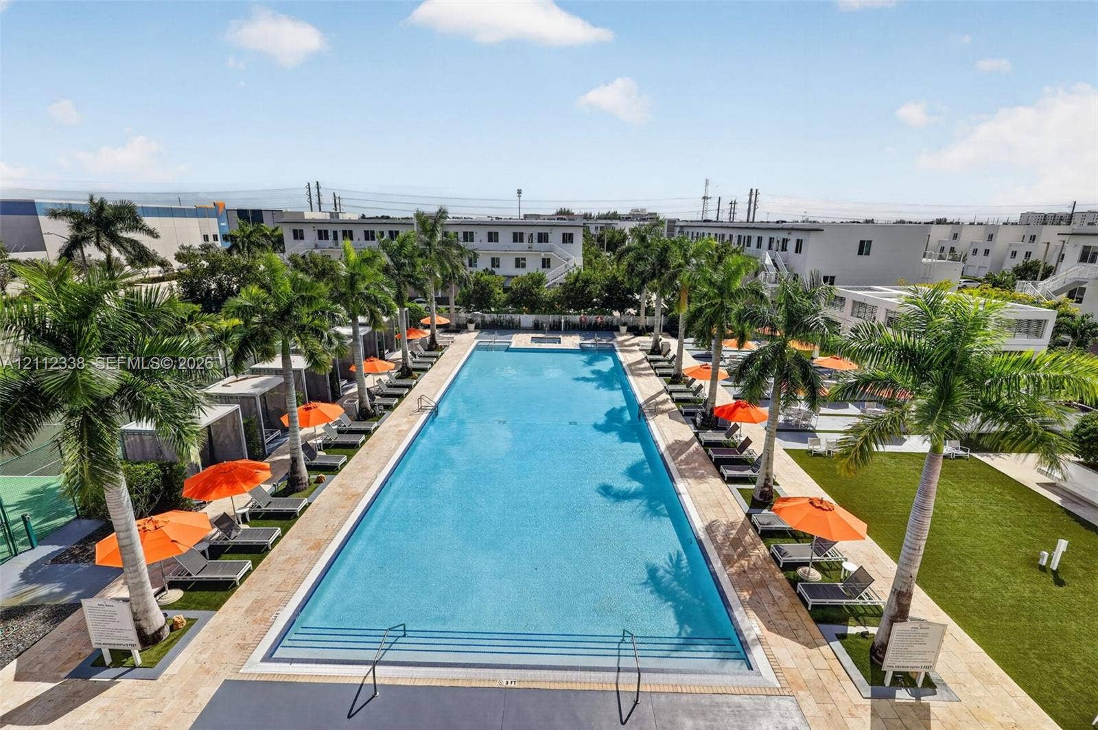10305 NW 63rd Terrace, #102, Doral, FL 33178 Rectangular swimming pool featuring a stone-tile deck, integrated stairs, perimeter palm trees, and artificial turf lawn space