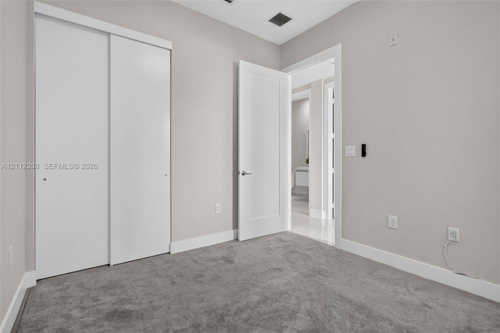 10305 NW 63rd Terrace, #102, Doral, FL 33178 Room featuring neutral wall tones, plush wall-to-wall carpeting, white sliding closet doors, and a solid-core hinged interior door