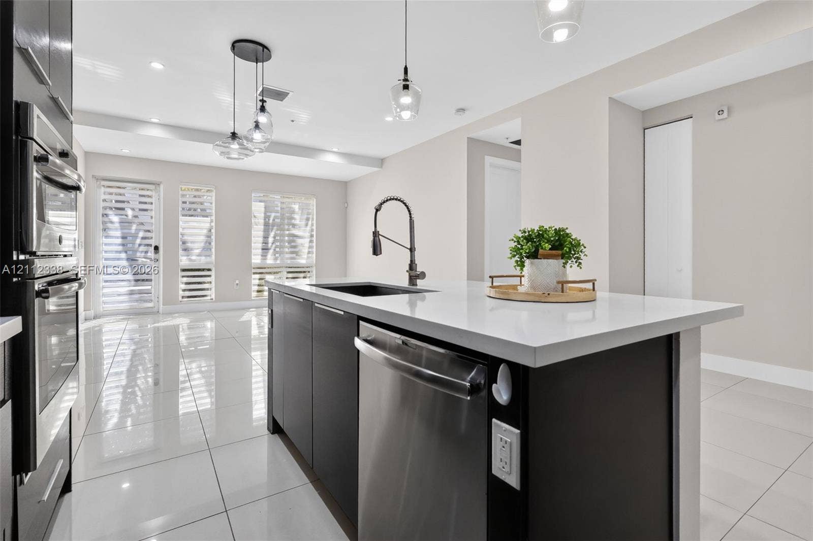 10305 NW 63rd Terrace, #102, Doral, FL 33178 Kitchen island featuring a stone-surface countertop, dark cabinetry, an undermount sink, a pull-down faucet, and a stainless steel dishwasher
