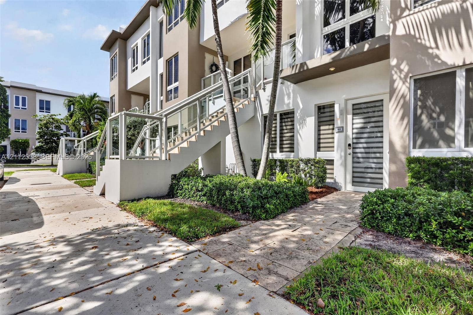 10305 NW 63rd Terrace, #102, Doral, FL 33178 Multi-story exterior featuring a stone-paver walkway, staircase with glass-panel railing, and large windows with horizontal blinds