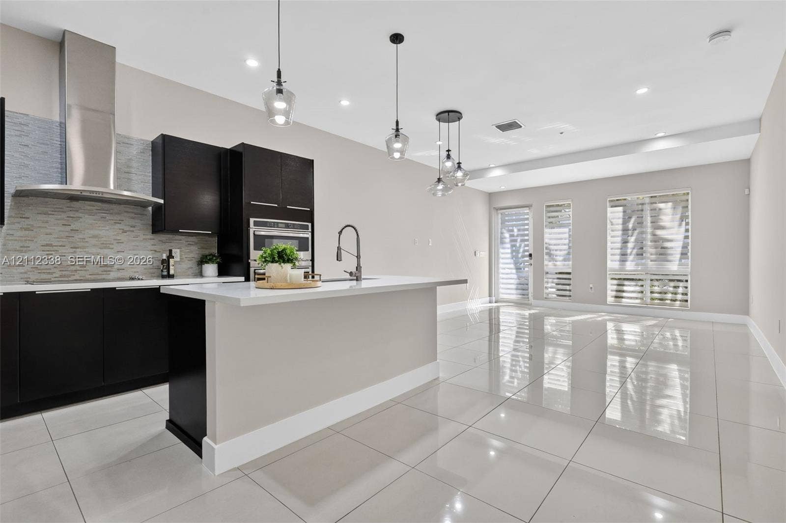 10305 NW 63rd Terrace, #102, Doral, FL 33178 Kitchen featuring dark cabinetry, quartz countertops, a stone-tiled backsplash, stainless steel range hood, and polished tile flooring