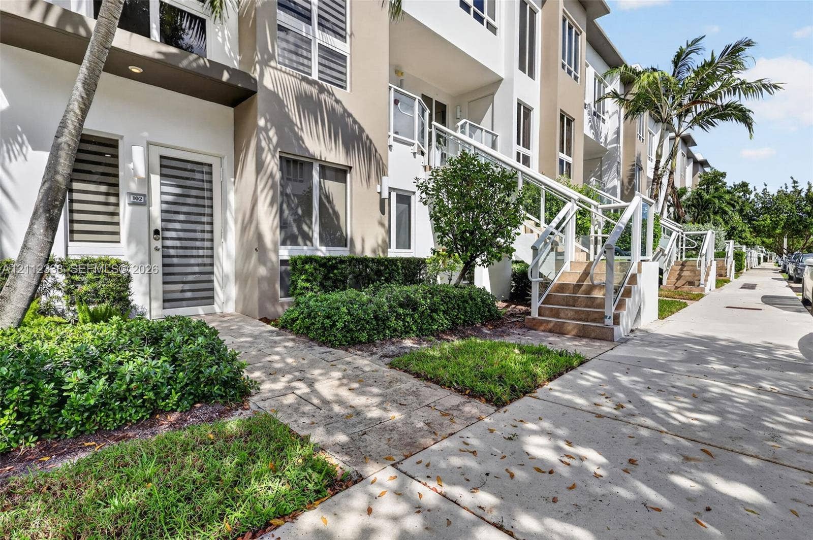 10305 NW 63rd Terrace, #102, Doral, FL 33178 Multi-level exterior featuring a smooth stucco facade, elevated concrete staircase with glass railings, stone-paver walkways, and manicured landscaping
