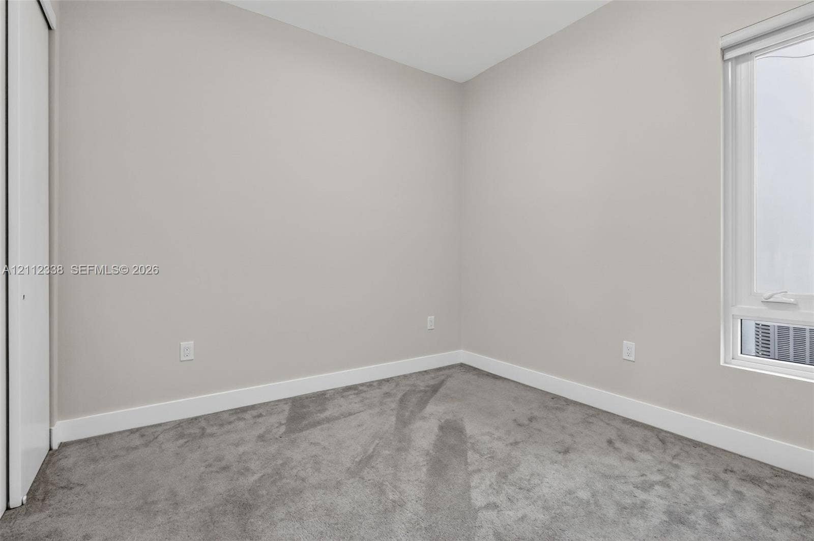 10305 NW 63rd Terrace, #102, Doral, FL 33178 Neutral-toned interior space featuring soft wall-to-wall carpeting, crisp white walls, and a window with an integrated roller shade