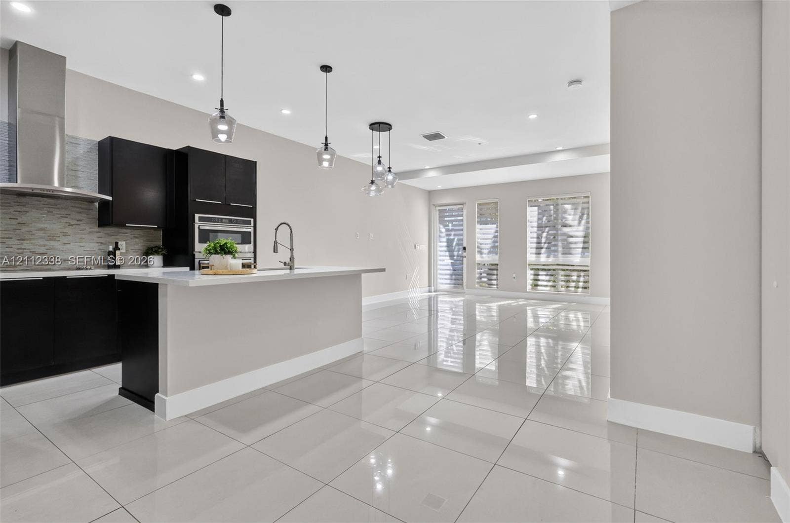 10305 NW 63rd Terrace, #102, Doral, FL 33178 Modern kitchen featuring high-gloss cabinetry, a central island with a solid surface countertop, stainless steel appliances, polished tile flooring, and glass pendant lighting