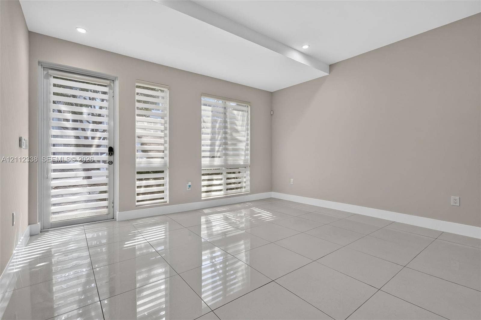 10305 NW 63rd Terrace, #102, Doral, FL 33178 Neutral-toned interior featuring large-format polished tile flooring, recessed ceiling lighting, a glass-panel exterior door, and multiple windows with adjustable roller shades