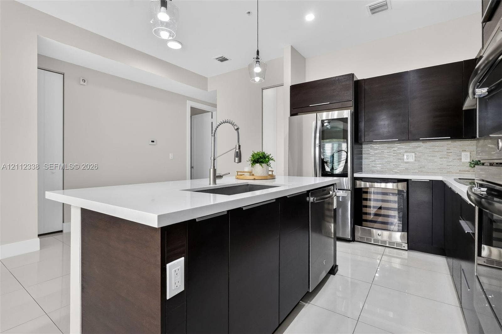10305 NW 63rd Terrace, #102, Doral, FL 33178 Kitchen featuring a central island with a solid surface countertop, dark-finish cabinetry, stainless steel appliances, a built-in wine refrigerator, and polished floor tile