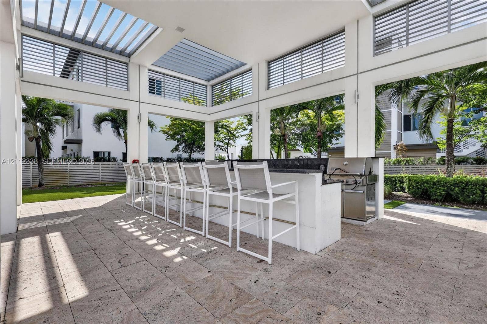 10305 NW 63rd Terrace, #102, Doral, FL 33178 Covered outdoor kitchen featuring a stone-topped bar, stainless steel grill, horizontal slat ceiling panels, and natural stone paver flooring