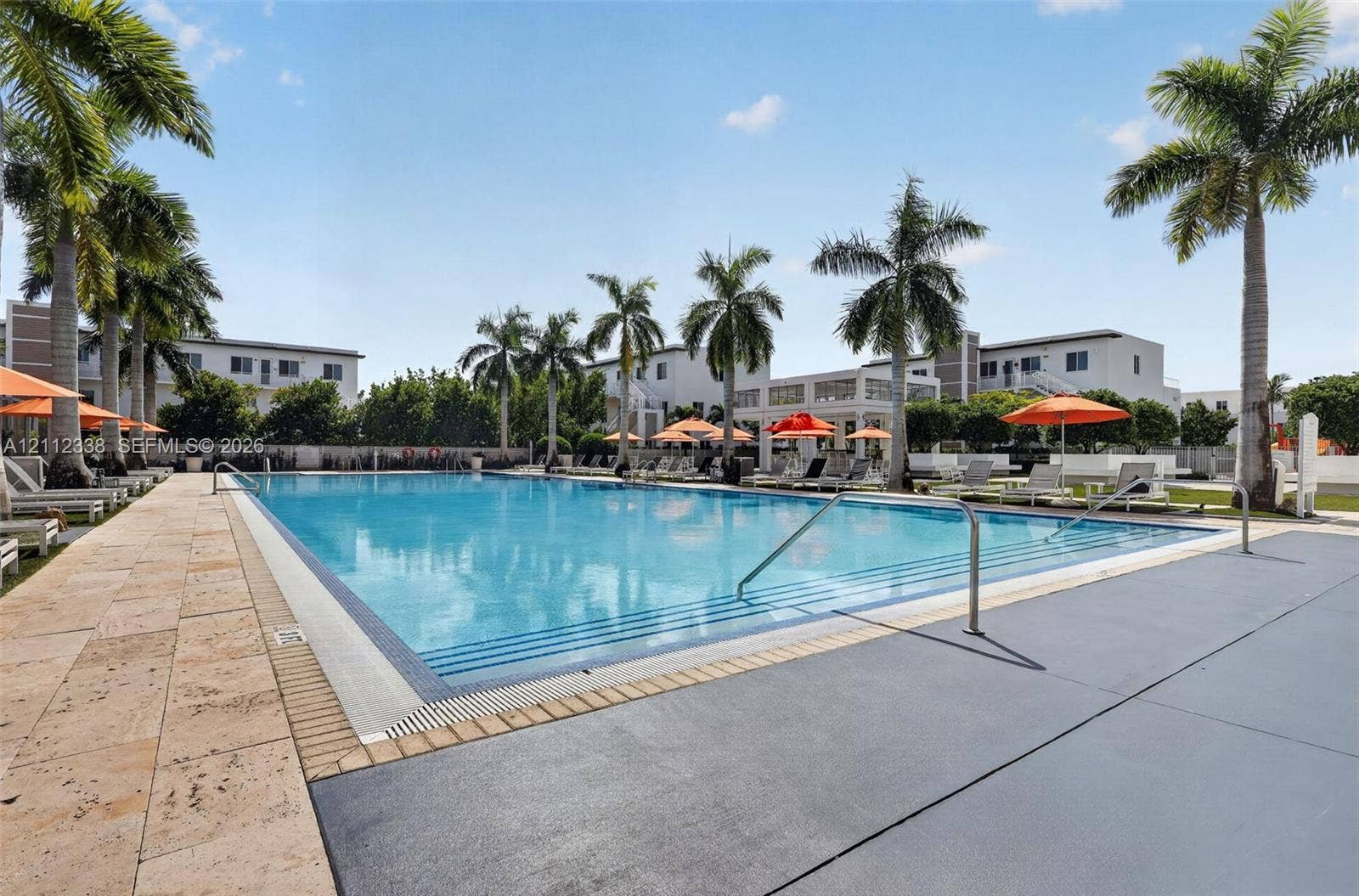 10305 NW 63rd Terrace, #102, Doral, FL 33178 Rectangular swimming pool featuring a tiled waterline, built-in steps with stainless steel handrails, expansive stone deck, and mature palm trees
