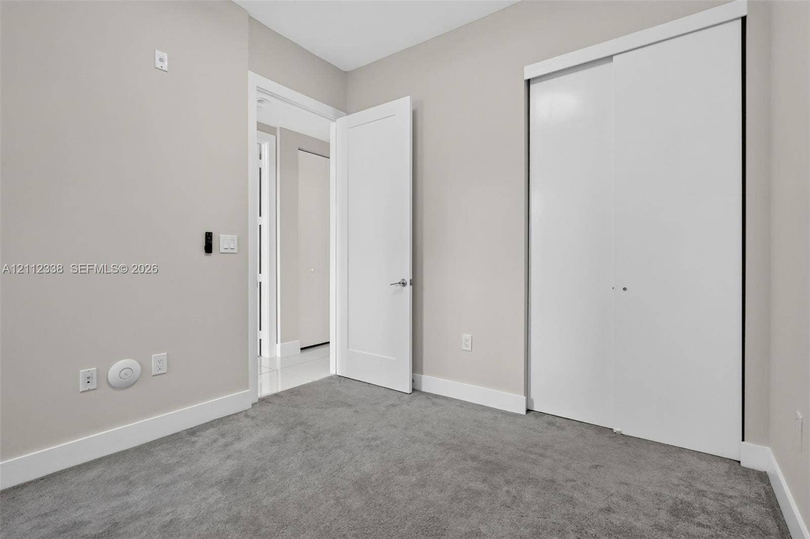 10305 NW 63rd Terrace, #102, Doral, FL 33178 Interior space featuring plush neutral carpeting, smooth-finish walls, a solid-core swing door with brushed metal hardware, and a sliding-panel closet with white finishes