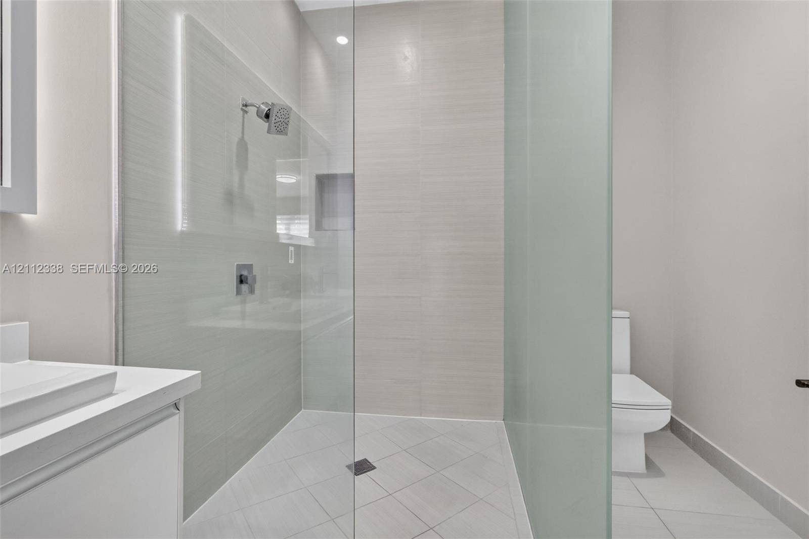 10305 NW 63rd Terrace, #102, Doral, FL 33178 Walk-in shower featuring glass enclosure, wall-mounted shower head, recessed shelving, and tiled flooring