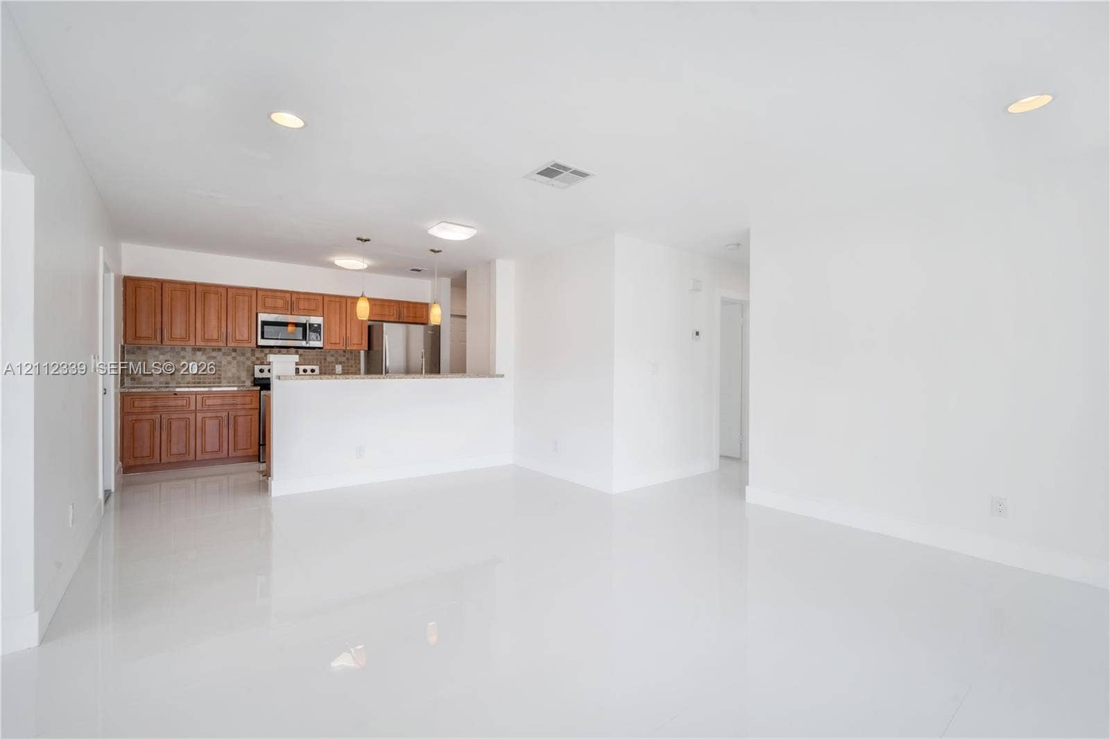8901 SW 149th Terrace, #n/a, Palmetto Bay, Palmetto Bay, FL 33176 Kitchen area featuring wood cabinetry, stone-tiled backsplash, breakfast bar with a granite countertop, tiled backsplash , recessed lighting, and white tile flooring throughout