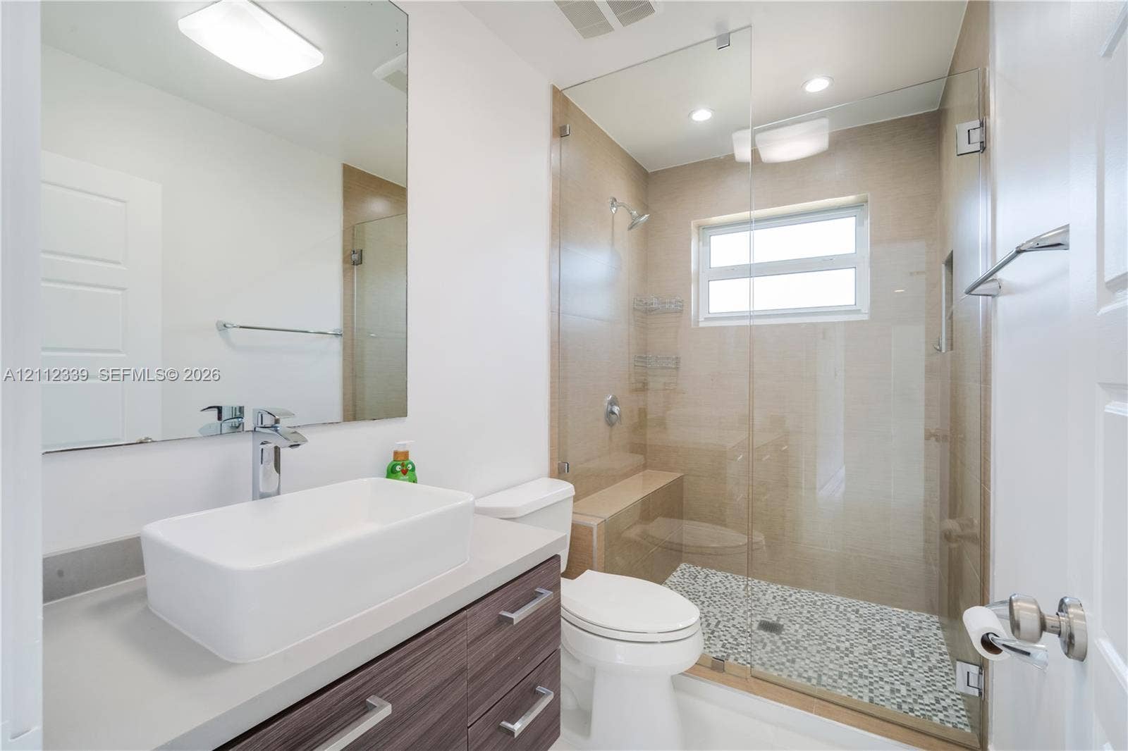 8901 SW 149th Terrace, #n/a, Palmetto Bay, Palmetto Bay, FL 33176 Bathroom featuring a vanity with a rectangular vessel sink, wood-finish cabinetry, a glass-enclosed shower with mosaic tile flooring, built-in shower seating, and a large wall-mounted mirror
