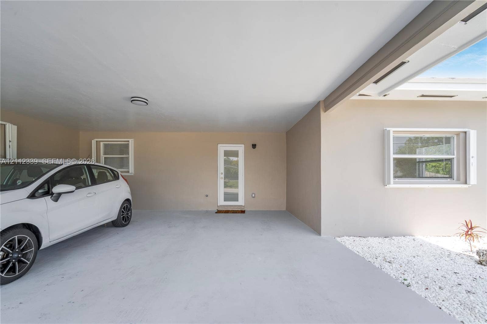 8901 SW 149th Terrace, #n/a, Palmetto Bay, Palmetto Bay, FL 33176 Covered carport for 1 car , featuring a smooth concrete floor, exterior wall lighting, and a glass-paneled entry door