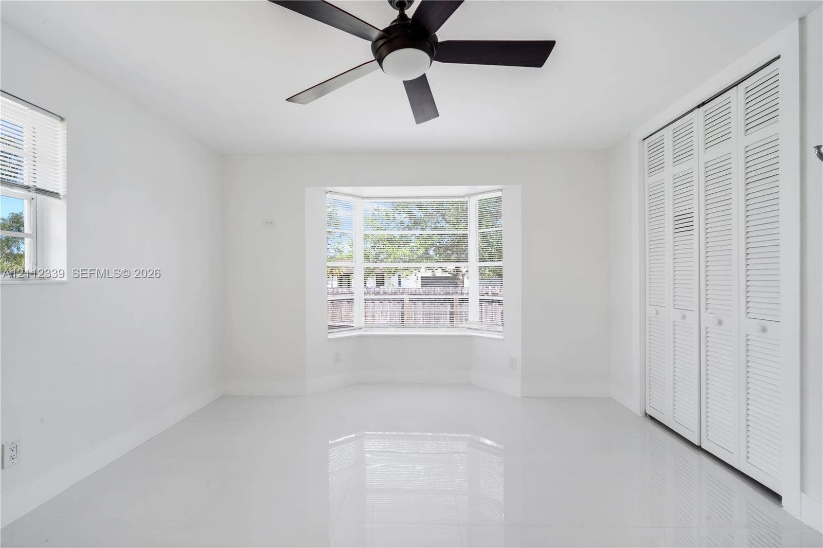 8901 SW 149th Terrace, #n/a, Palmetto Bay, Palmetto Bay, FL 33176 Room featuring large-format tile flooring, a multi-pane bay window, white louvered-style closet doors, and a ceiling-mounted fan with integrated lighting