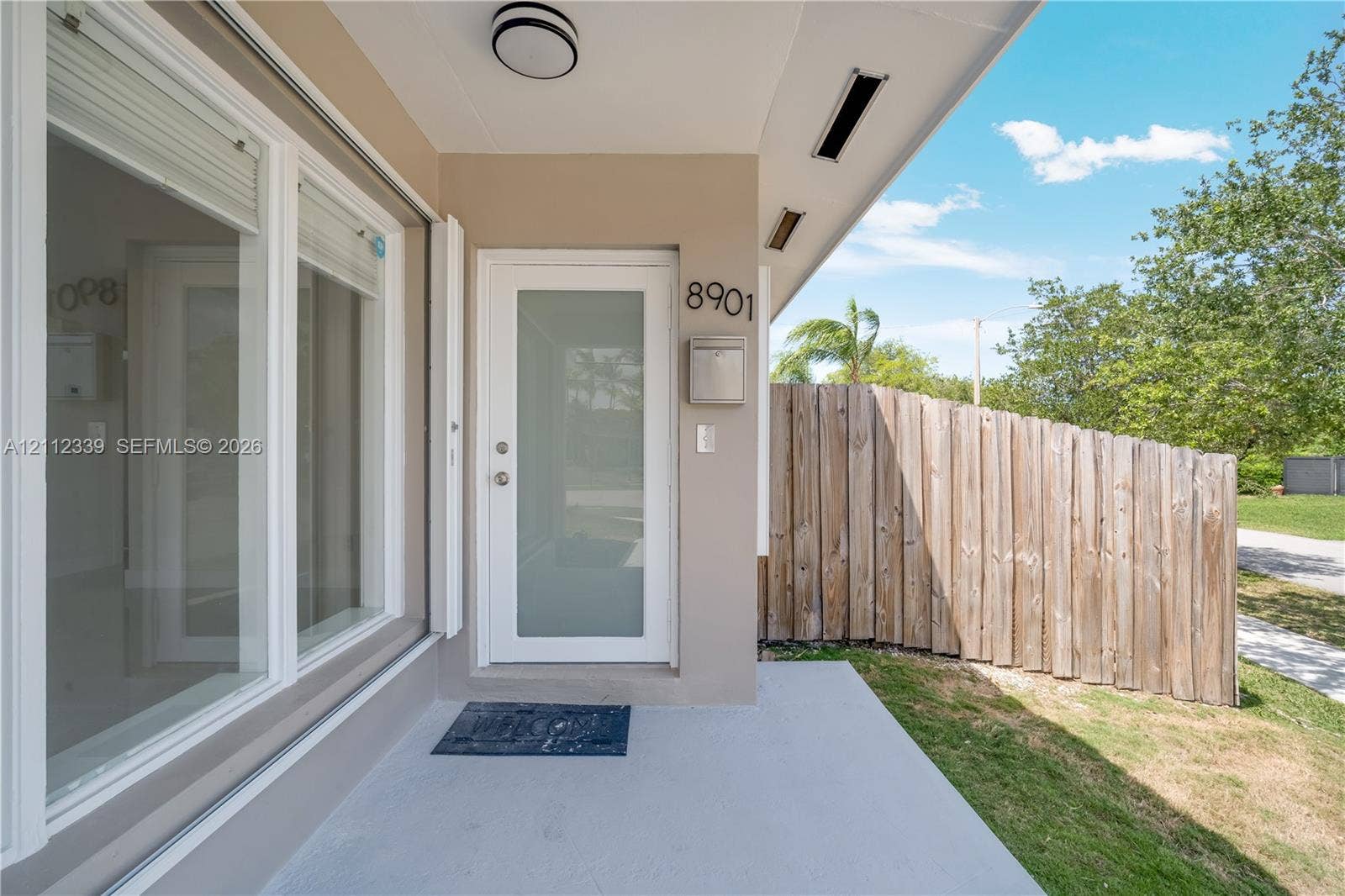 8901 SW 149th Terrace, #n/a, Palmetto Bay, Palmetto Bay, FL 33176 Covered porch entry featuring a frosted glass panel front door, recessed lighting, exterior wall-mounted mailbox, and wood-slat privacy fencing