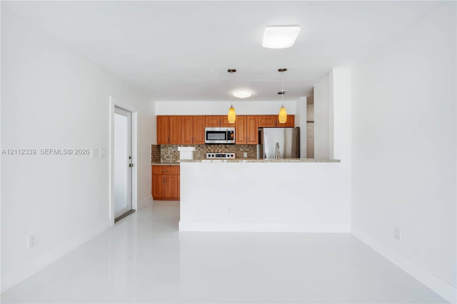 8901 SW 149th Terrace, #n/a, Palmetto Bay, Palmetto Bay, FL 33176 Renovated kitchen featuring wood cabinetry, granite countertops, a tiled backsplash, stainless steel appliances, and two hanging pendant lights