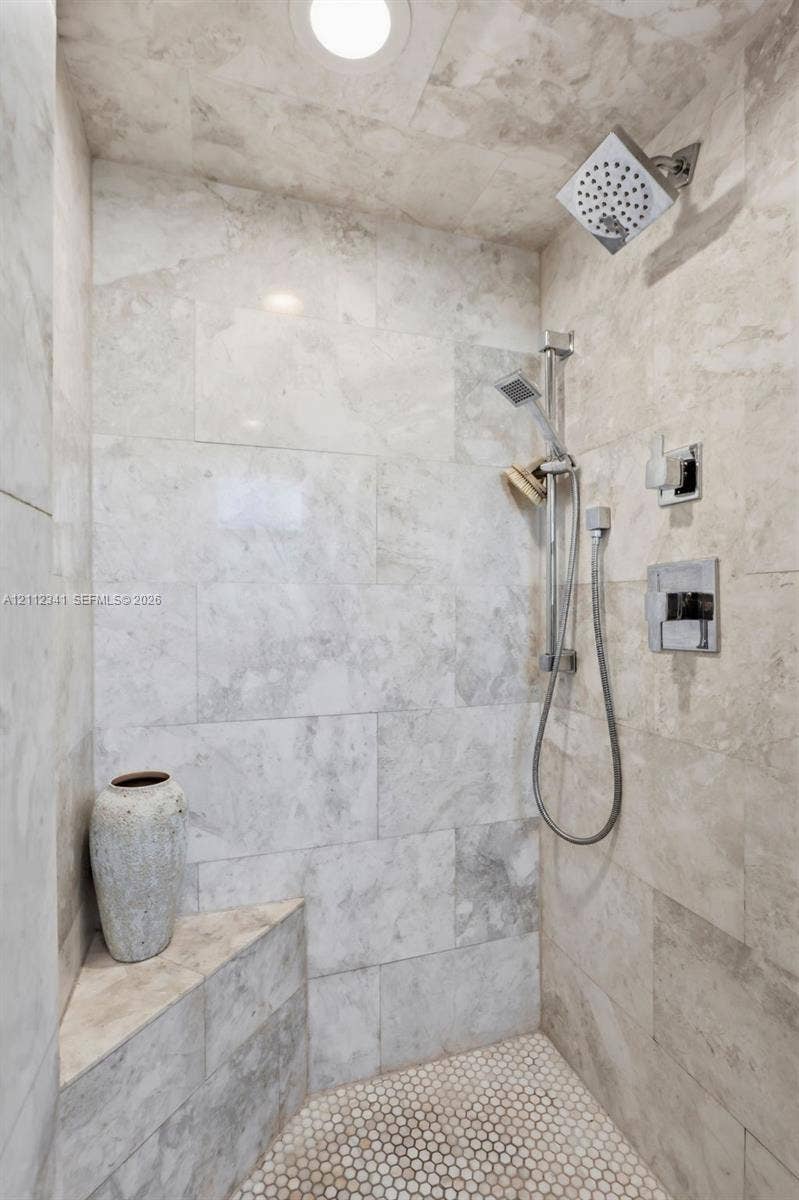 1617 SE 15th Street, #401, Fort Lauderdale, FL 33316 Walk-in shower featuring large-format stone tile wall cladding, hexagonal tile flooring, a built-in corner bench, a square rain-style showerhead, and a multi-function handheld shower attachment with polished chrome hardware