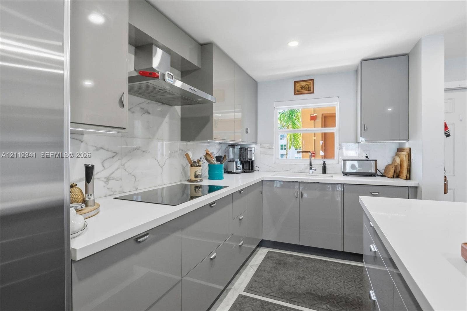 1617 SE 15th Street, #401, Fort Lauderdale, FL 33316 Kitchen featuring high-gloss gray slab cabinetry, solid-surface countertops, full-height stone-patterned backsplash, stainless steel range hood, and integrated cooktop