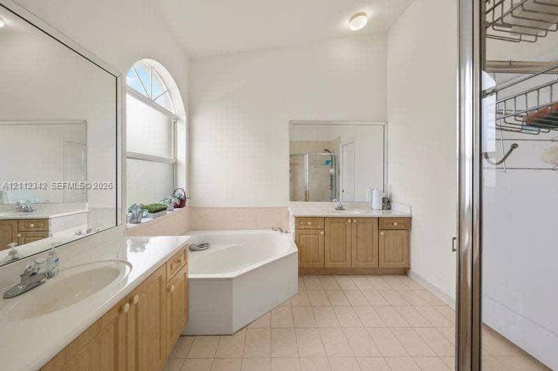 Bathroom featuring dual wooden vanities with white countertops, a deep corner soaking tub, a large arched window, and full-length mirrors