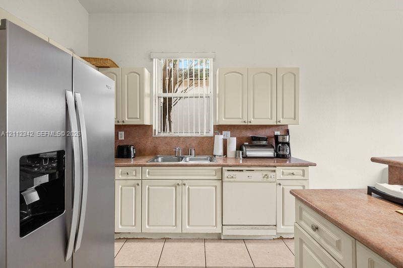 Kitchen featuring off-white cabinetry, stainless steel side-by-side refrigerator, tile backsplash, solid-surface countertops, and ceramic tile flooring