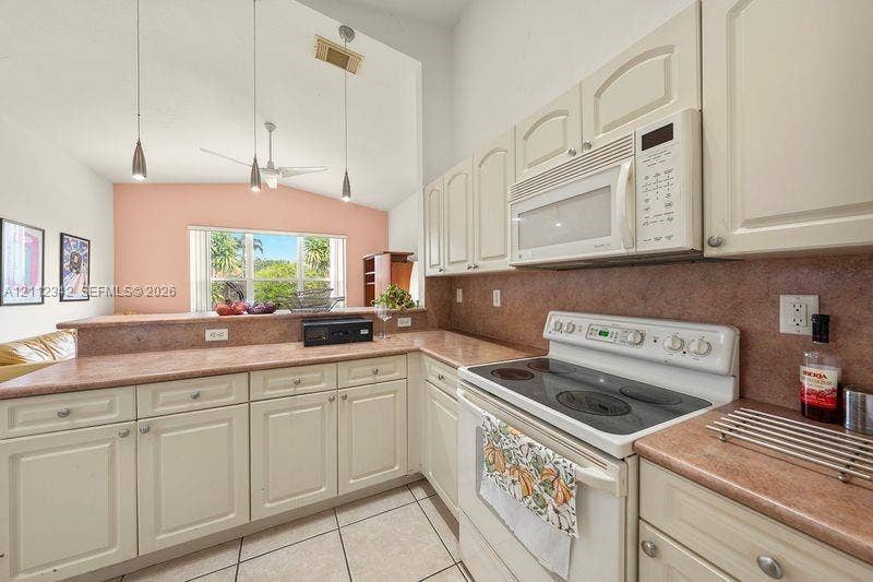 Kitchen featuring off-white cabinetry, stone-texture countertops, tile flooring, built-in microwave, and pendant lighting