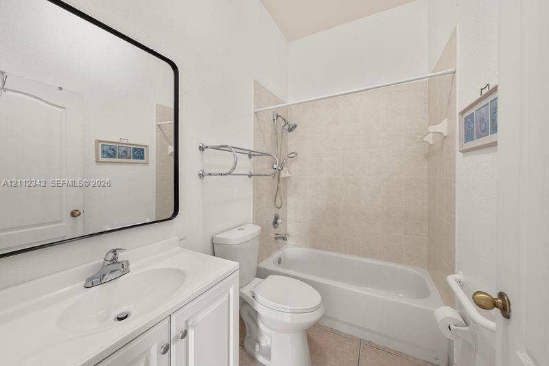 Bathroom featuring a white vanity with integrated basin, polished chrome faucet, black-framed mirror, and a tub-shower combination with ceramic tile surround