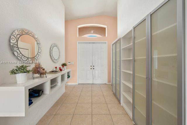 Foyer featuring double-entry doors, vaulted ceiling, arched transom window, ceramic tile flooring, and extensive built-in cabinetry with frosted glass doors