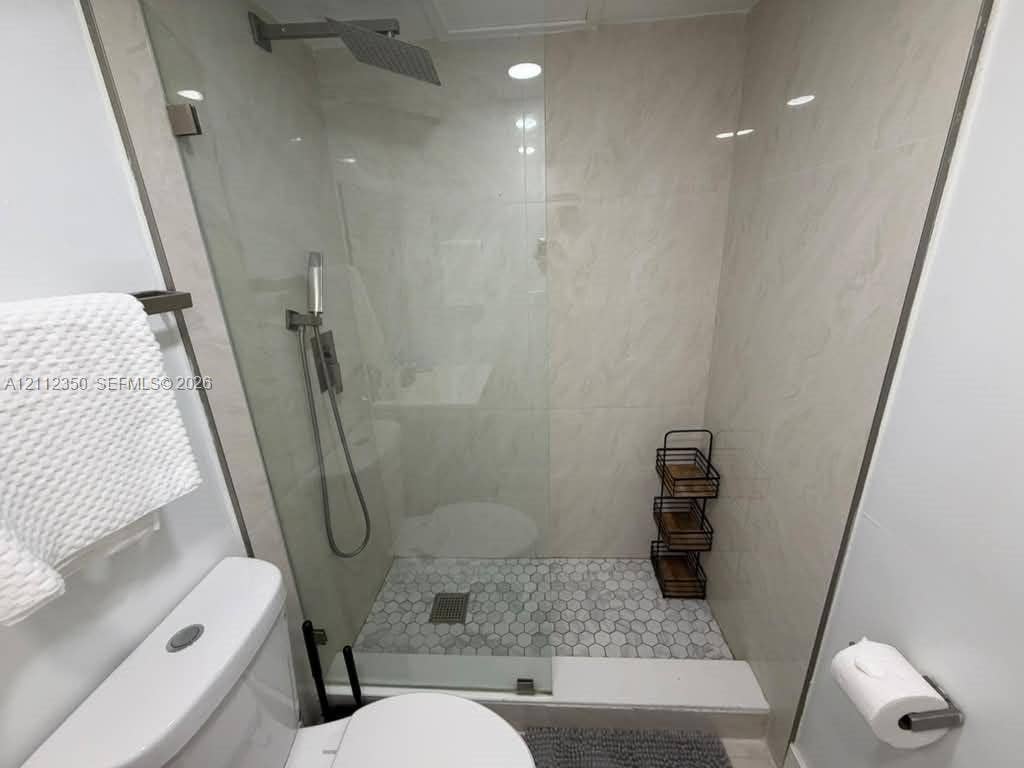 Walk-in shower featuring large-format wall tile, hexagonal floor tile, glass enclosure, and ceiling-mounted rain showerhead with a secondary handheld sprayer