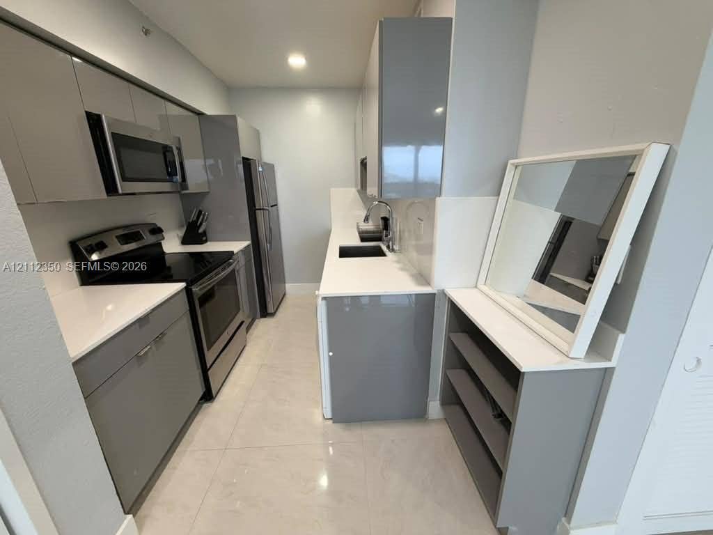 Galley kitchen featuring high-gloss grey cabinetry, stone-finish countertops, stainless steel appliances, and tile flooring