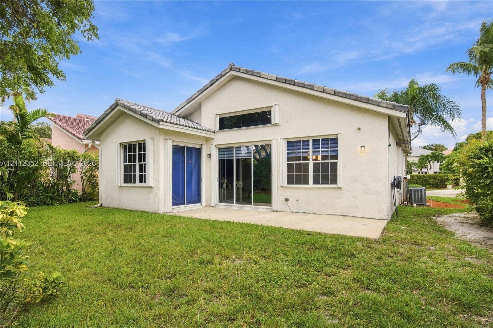 2880 NW 75th Avenue, Margate, FL 33063 Stucco exterior featuring a concrete tile roof, rear concrete patio, sliding glass doors, and a multi-paned transom window