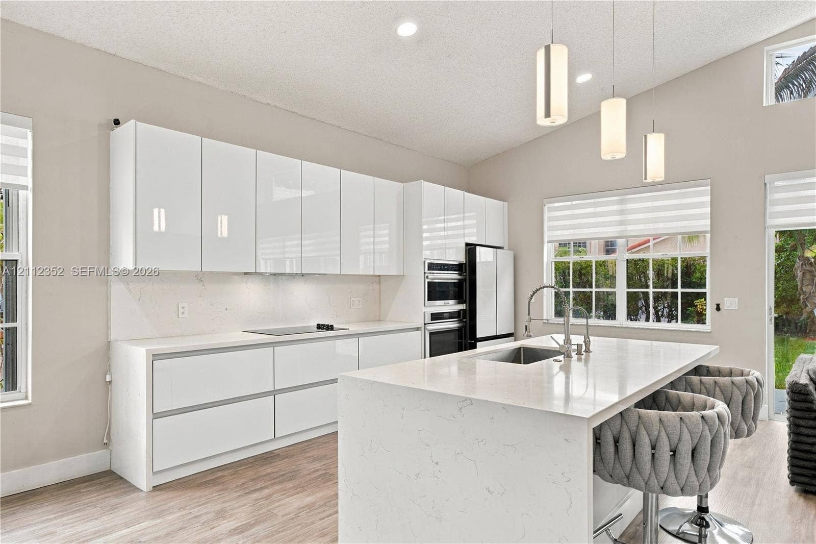 2880 NW 75th Avenue, Margate, FL 33063 Modern kitchen featuring flat-panel white cabinetry, stone-surface countertops, a waterfall-edge center island with an undermount sink, built-in double wall ovens, and pendant lighting
