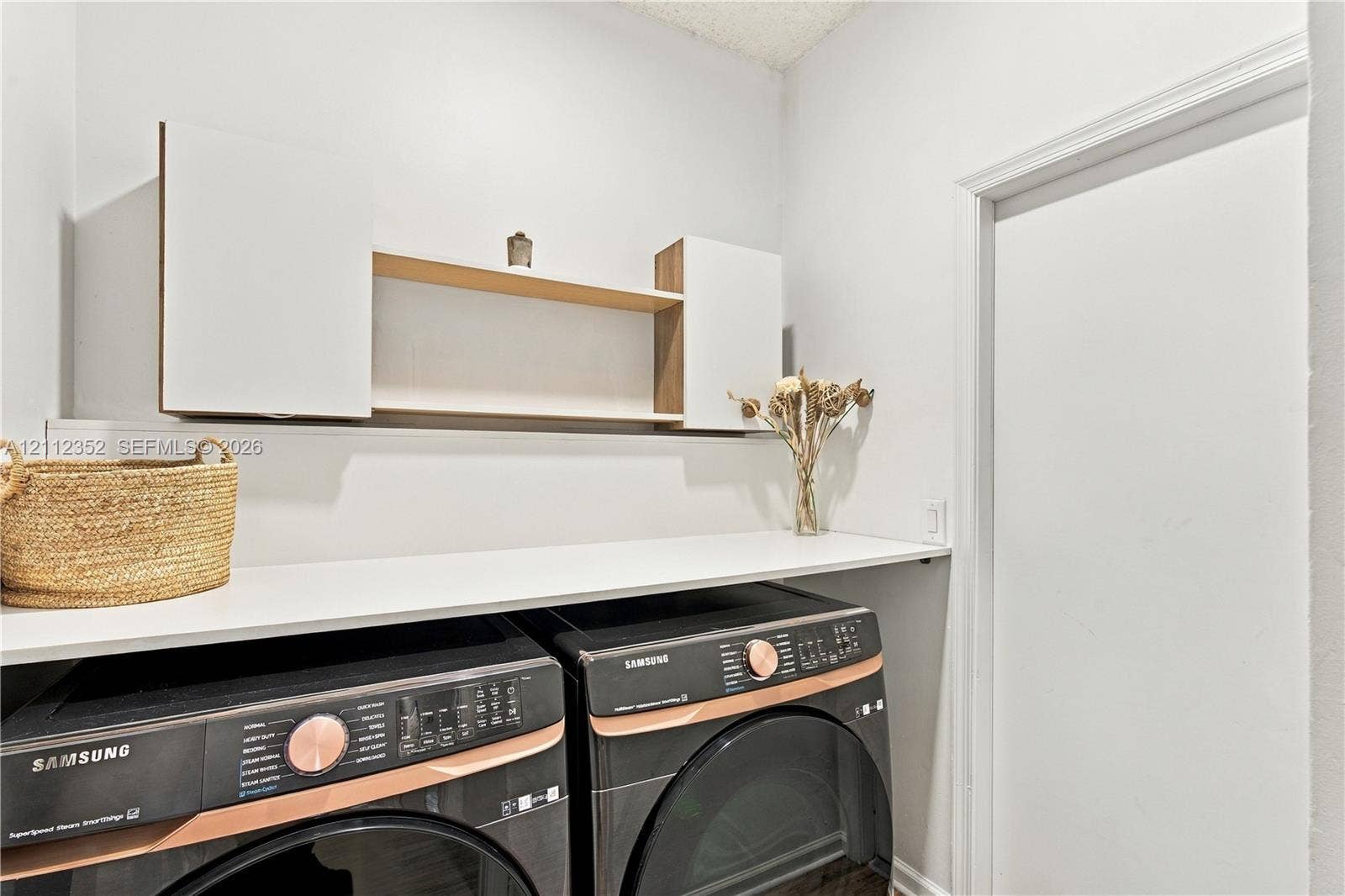 2880 NW 75th Avenue, Margate, FL 33063 Laundry area featuring built-in white cabinetry, an open wood-finish shelf, and a white countertop above laundry appliances